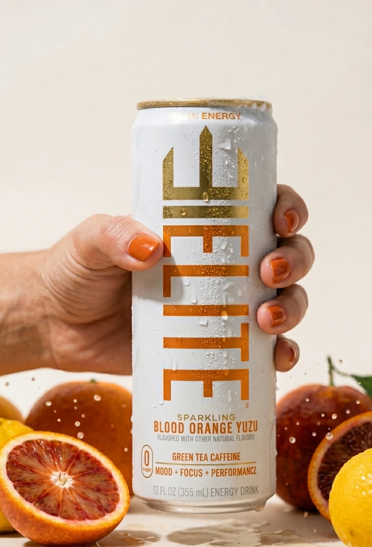 Hand holding an ice-cold ELITE Blood Orange Yuzu can among fresh citrus
